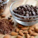 A bowl of the best Amaretto baking chips on a wooden countertop, surrounded by almonds and cocoa powder, perfect for adding rich almond flavor to baked goods.